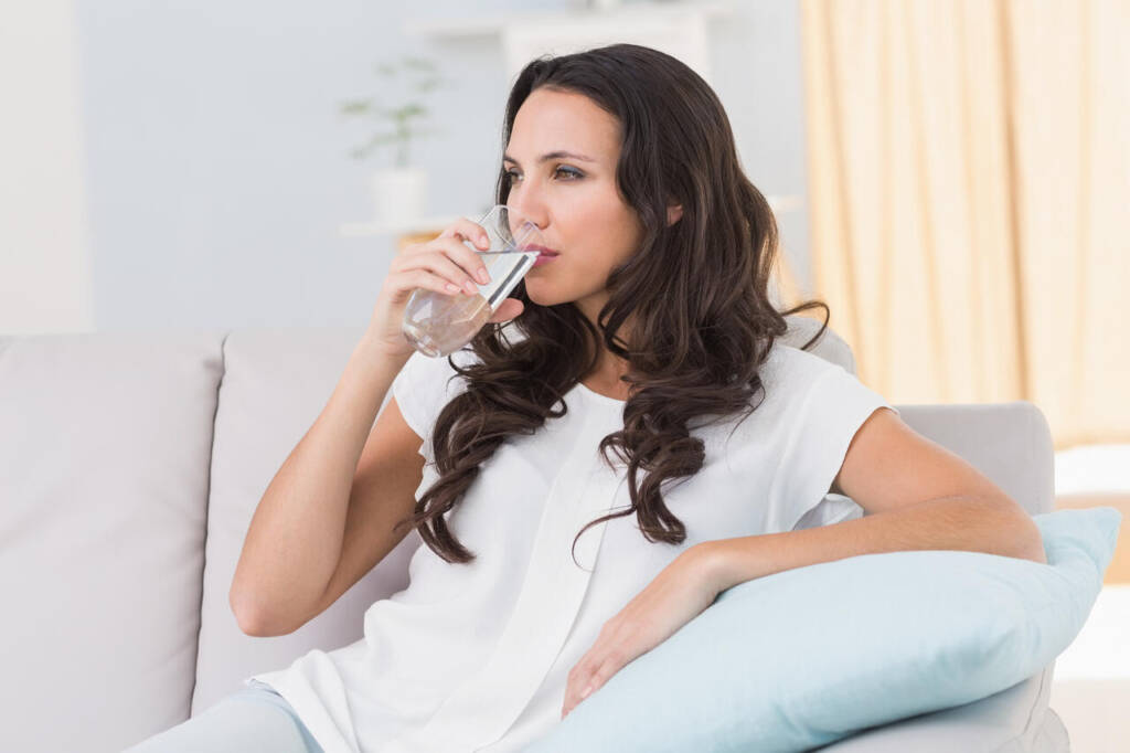 Pretty,Brunette,Drinking,Water,On,Couch,At,Home,In,The