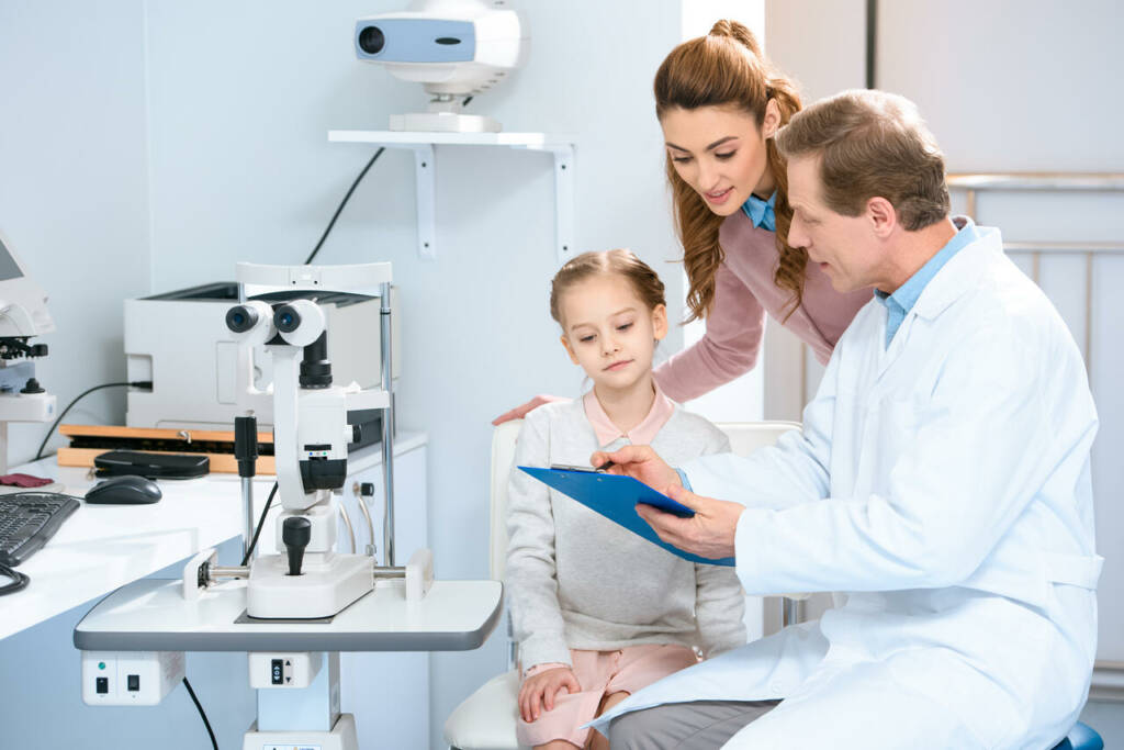 Mother,And,Daughter,Looking,At,Clipboard,In,Ophthalmologist,Consulting,Room